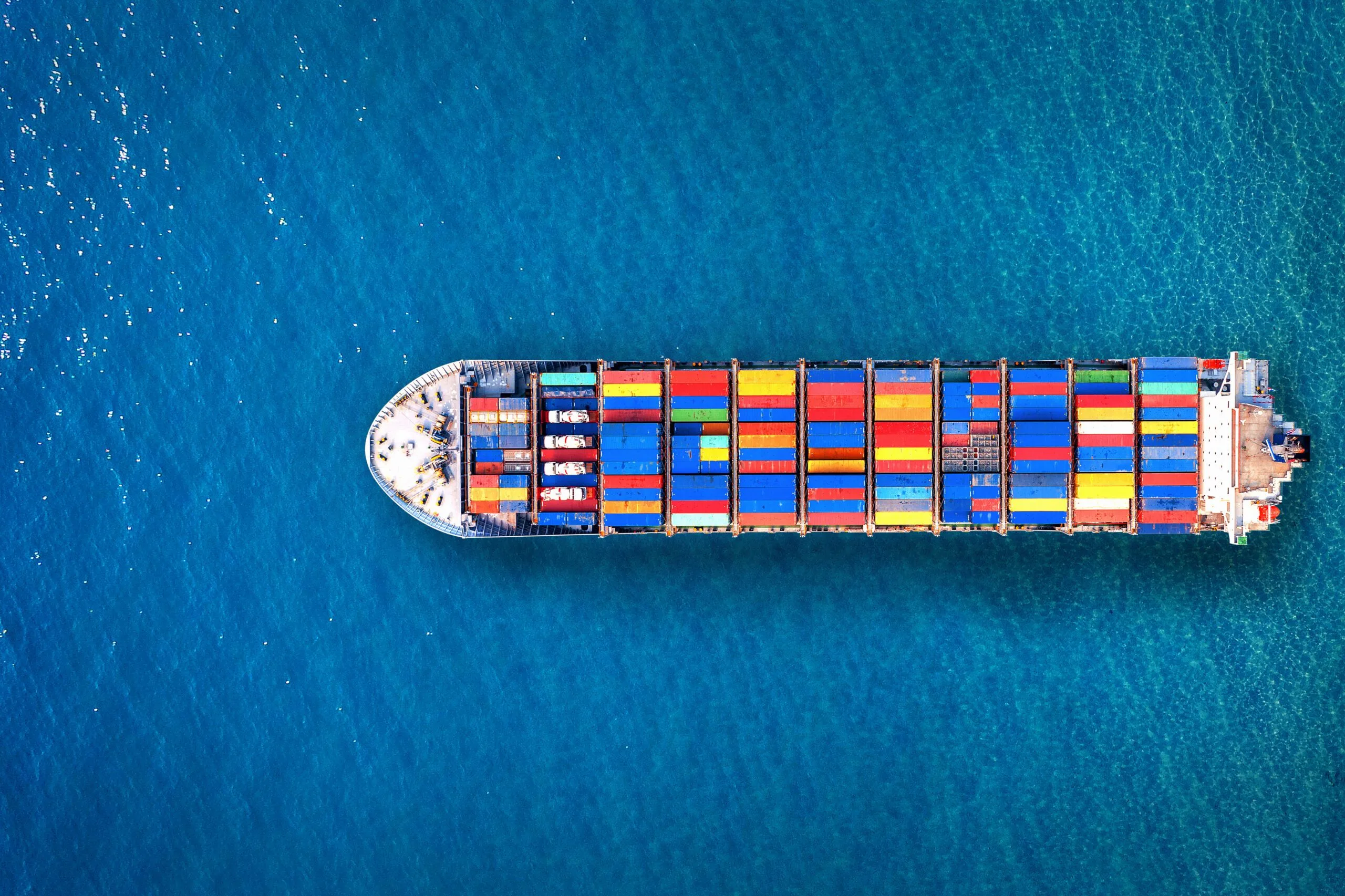 Luftaufnahme eines Containerschiffs auf dem Meer, das die Bedeutung der globalen Lieferketten und des internationalen Handels symbolisiert.